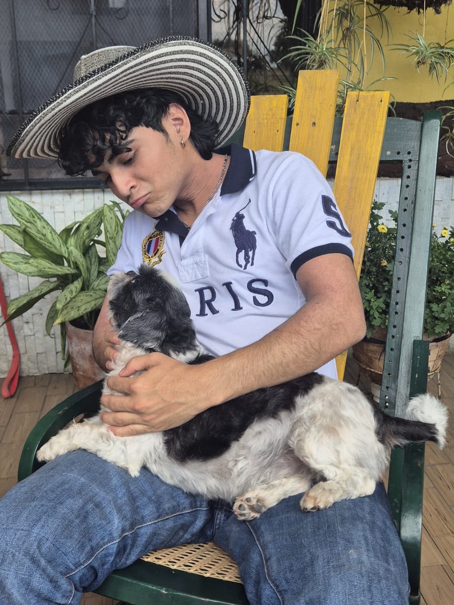 Me in a striped sombrero vueltiao on a rocking chair, cuddling a black-and-white dog